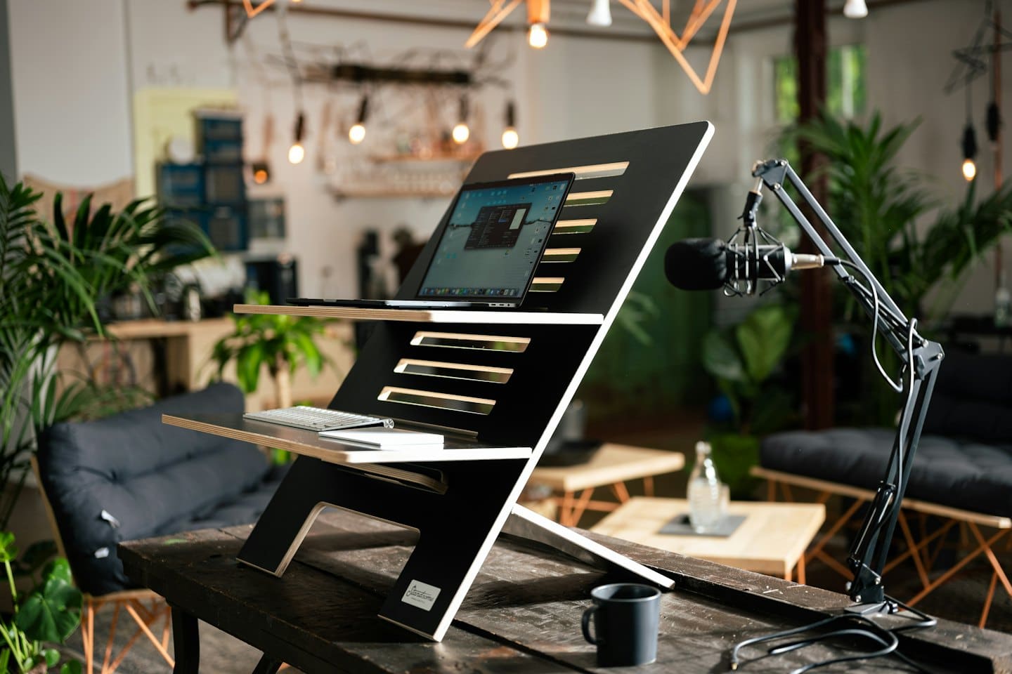 Wooden standing desk with laptop and microphone for recording.