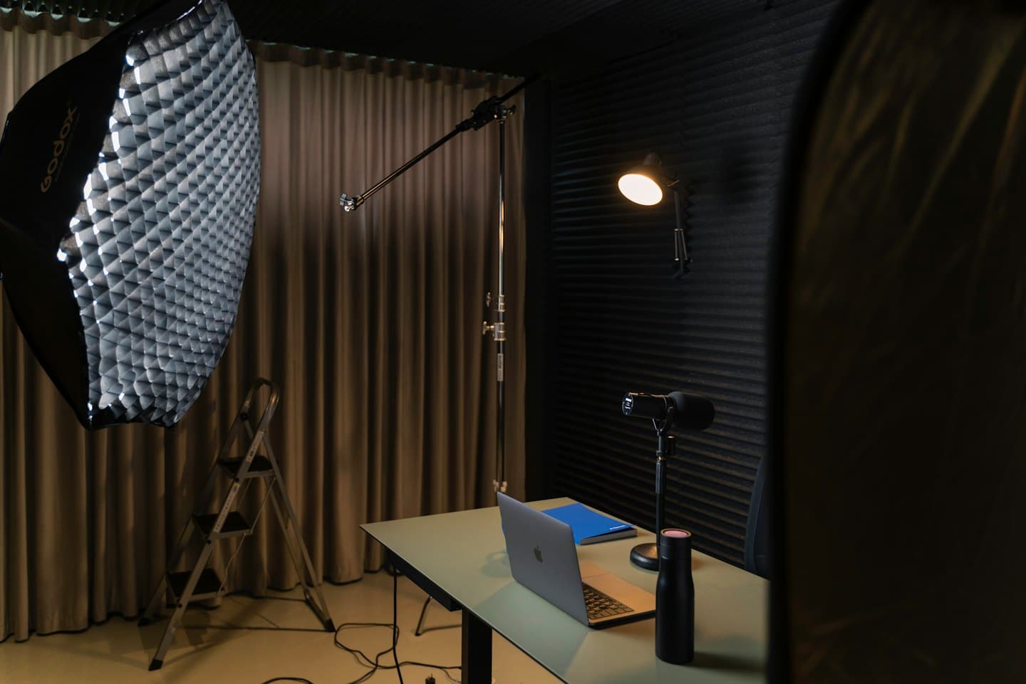 Desk with laptop, microphone, and softbox in a studio.